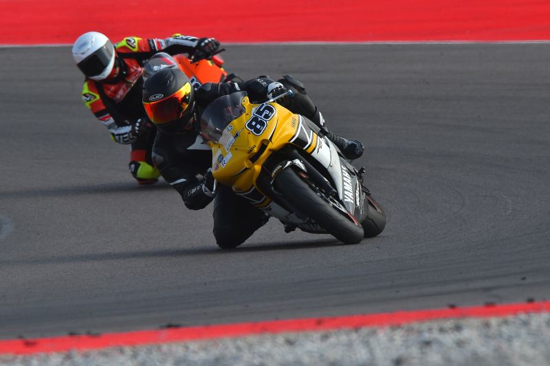 Two bikes leaning into a corner on a track day, the one in front a yellow Yamaha carrying number 85